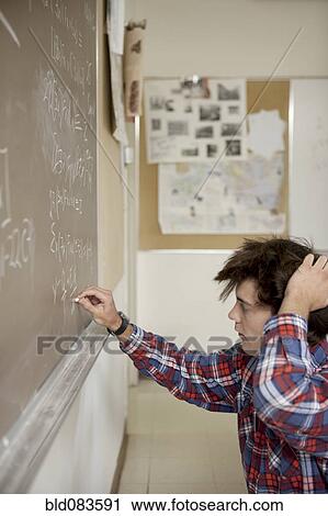 Stock Image - Caucasian student writing on blackboard. Fotosearch