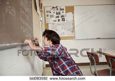 Stock Image - Caucasian student writing on blackboard. Fotosearch