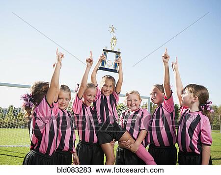 Stock Image - Cheering girl soccer players posing with trophy. Fotosearch