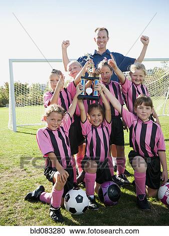Stock Image - Coach and girl soccer players posing with trophy. Fotosearch