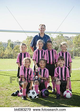 Stock Photo - Coach and girl soccer players posing with trophy. Fotosearch