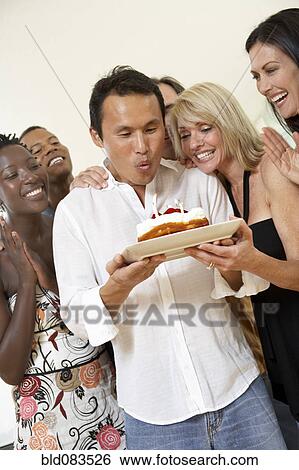 Stock Photograph - Friends watching man blow out birthday candles. Fotosearch