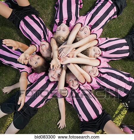 Stock Image - Girl soccer players laying in circle with arms raised. Fotosearch