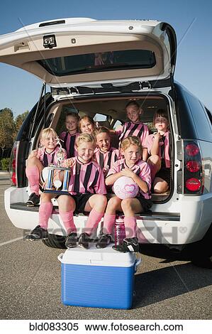 Stock Photography - Girl soccer players sitting in back of car with trophy. Fotosearch