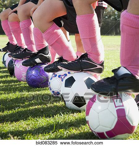 Stock Photography - Girl soccer players standing with feet on soccer balls. Fotosearch