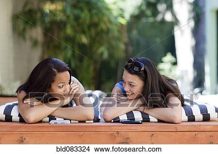 Picture - Girls laying on lounge chairs talking. Fotosearch