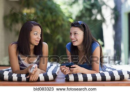 Stock Image - Girls laying on lounge chairs talking. Fotosearch