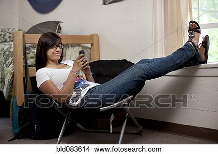 Picture - Hispanic woman hanging out in college dorm room. Fotosearch