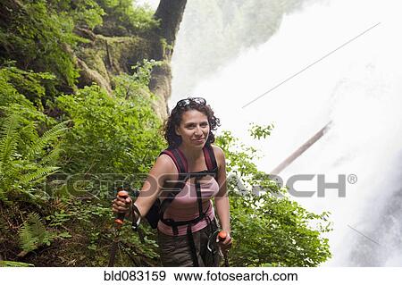 Stock Photo - Hispanic woman hiking in woods near waterfall. Fotosearch