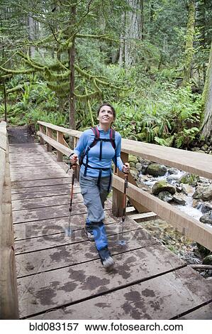 Stock Photo - Hispanic woman hiking over bridge in woods. Fotosearch