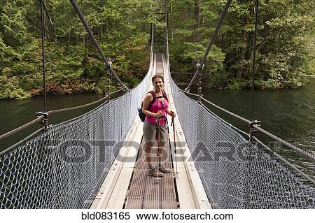 Stock Photography - Hispanic woman hiking over bridge in woods. Fotosearch