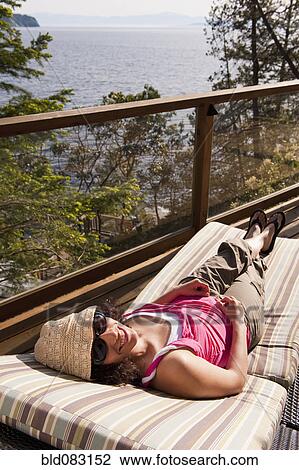 Stock Image - Hispanic woman laying on deck chair sunbathing. Fotosearch