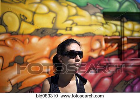 Stock Image - Hispanic woman standing near graffiti wall. Fotosearch