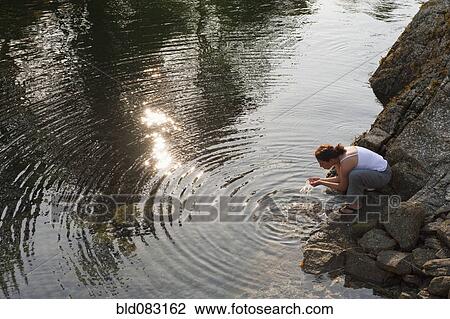 Stock Image - Hispanic woman washing face in lake. Fotosearch