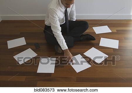 Stock Image - Mixed race businessman choosing paper on floor. Fotosearch