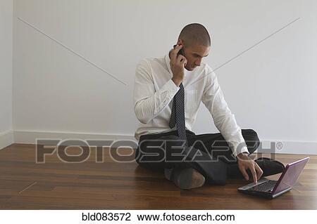 Stock Image - Mixed race businessman using laptop on floor. Fotosearch