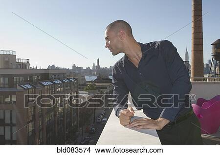 Picture - Mixed race man standing on urban balcony. Fotosearch
