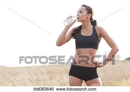 Stock Photograph - Serious mixed race woman in sportswear drinking water. Fotosearch