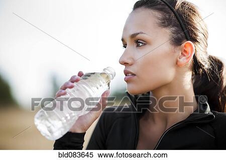 Stock Photography - Serious mixed race woman in sportswear drinking water. Fotosearch