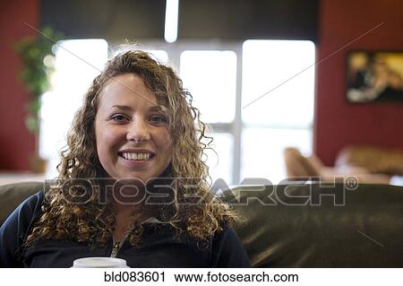Stock Image - Smiling Caucasian woman drinking coffee in cafe. Fotosearch
