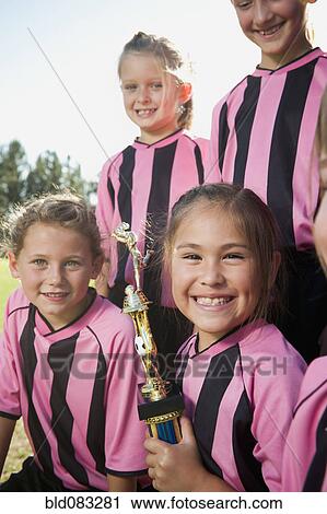 Stock Image - Smiling girl soccer players posing with trophy. Fotosearch