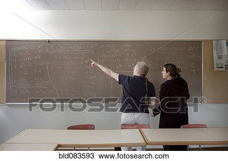 Stock Image - Teacher explaining arithmetic to student in classroom. Fotosearch
