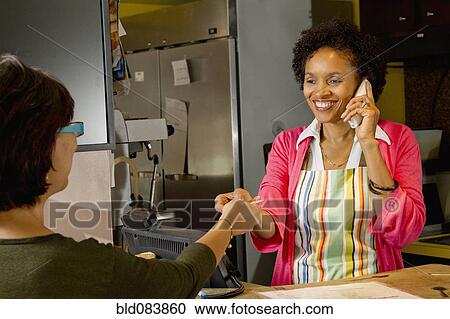 Stock Image - African American bakery owner taking customer's credit card. Fotosearch