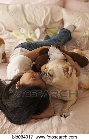 Stock Photo - Asian girl laying on bed with dog. Fotosearch