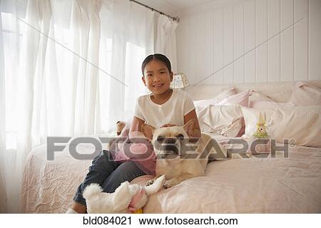Stock Image - Asian girl sitting on bed with dog. Fotosearch