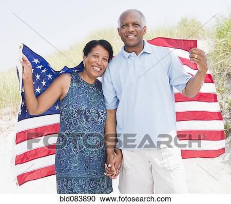 Stock Image - Black couple on beach wrapped in American flag. Fotosearch