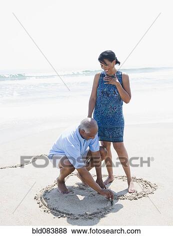 Stock Photo - Black man drawing heart on beach for wife. Fotosearch