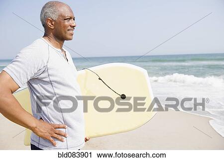 Black man holding body board on beach View Large Photo Image Stock Image - Black man holding body board on beach. Fotosearch
