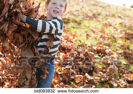 Stock Image - Caucasian boy playing with autumn leaves. Fotosearch