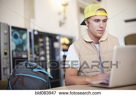 Stock Photo - Caucasian man using laptop in cafeteria. Fotosearch