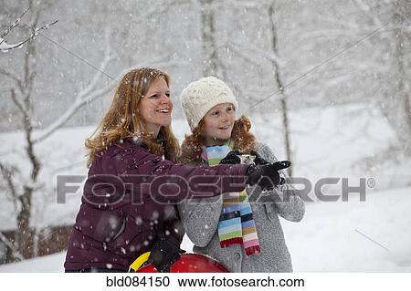 Stock Image - Caucasian mother and daughter standing in snow with sled. Fotosearch