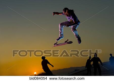Caucasian skateboarder doing stunt in mid-air at sunset View Large Photo Image Picture - Caucasian skateboarder doing stunt in mid-air at sunset. Fotosearch