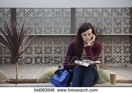Stock Photograph - Caucasian woman reading book outdoors. Fotosearch