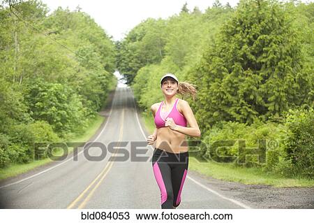 Stock Image - Caucasian woman running on remote road. Fotosearch