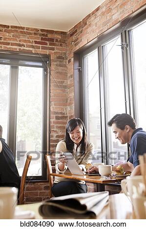 Stock Image - Chinese woman digital tablet to husband in cafe. Fotosearch