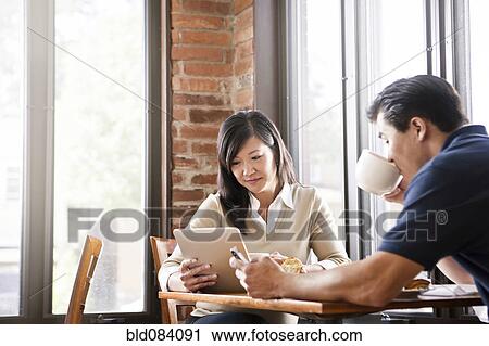 Stock Image - Chinese woman digital tablet to husband in cafe. Fotosearch