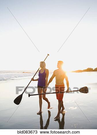 Couple walking on beach carrying paddles View Large Photo Image Stock Image - Couple walking on beach carrying paddles. Fotosearch