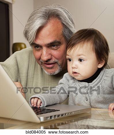 Stock Photography - Grandfather and granddaughter using laptop together. Fotosearch