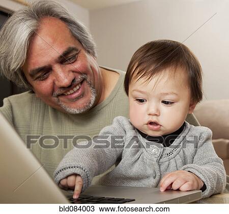Stock Image - Grandfather watching granddaughter using laptop. Fotosearch