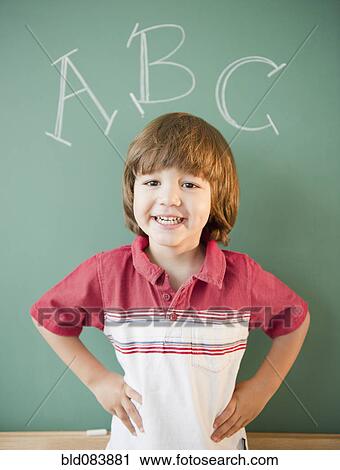 Stock Image - Hispanic boy standing underneath abc's on blackboard. Fotosearch