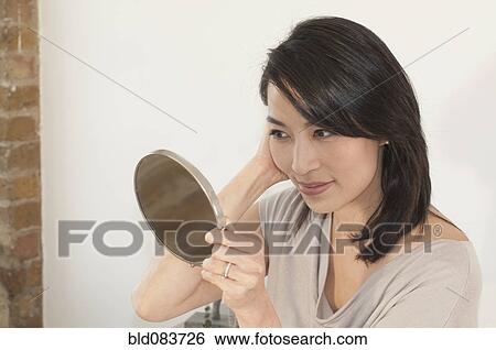 Stock Photograph - Korean woman looking in mirror. Fotosearch