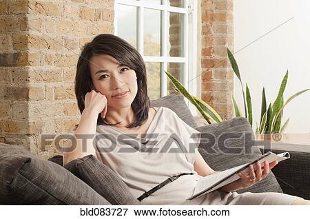 Korean Woman On Sofa Reading Magazine Stock Photo