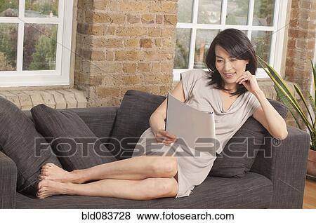Stock Photo - Korean woman on sofa reading magazine. Fotosearch