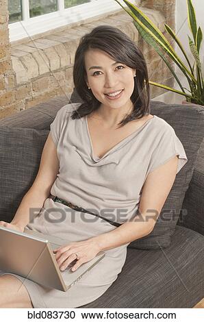 Stock Image - Korean woman on sofa using laptop. Fotosearch