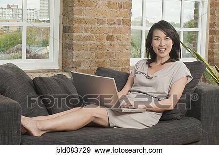Stock Photo - Korean woman on sofa using laptop. Fotosearch