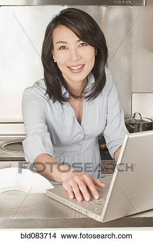 Korean woman using laptop in kitchen View Large Photo Image Picture - Korean woman using laptop in kitchen. Fotosearch